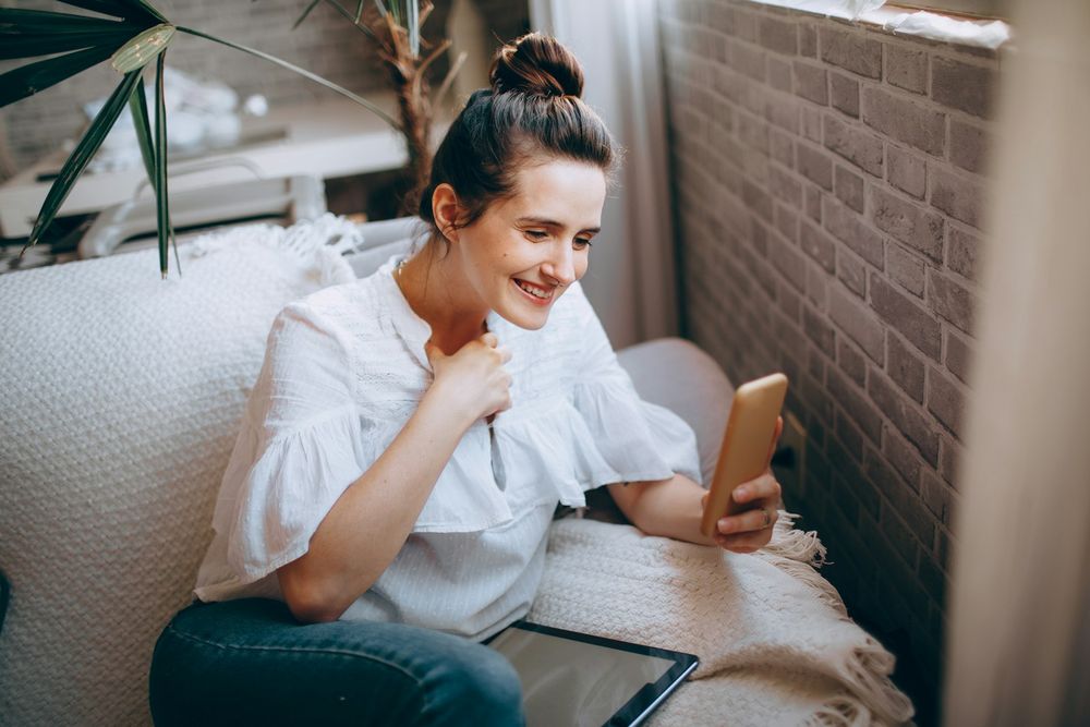 A woman on a sofa smiling at her phone.